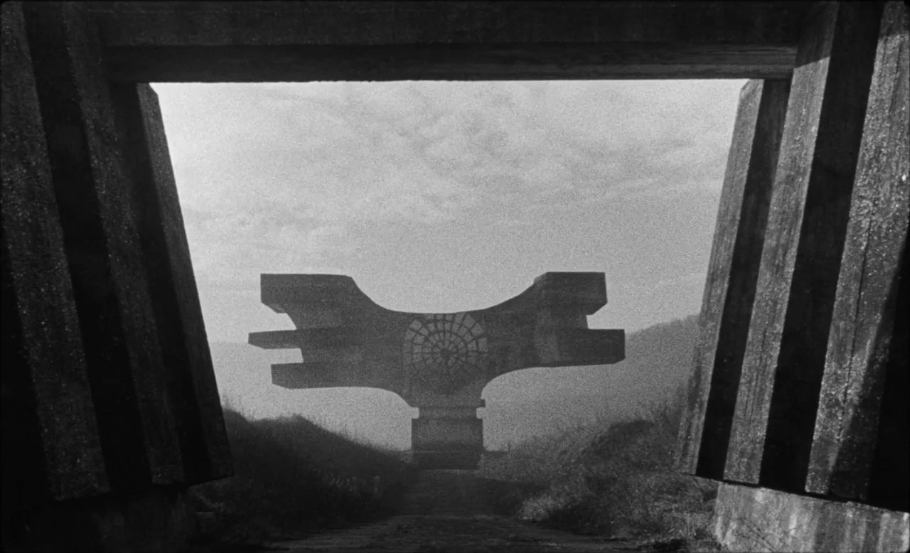 Last and First Men (2020) movie still: wide — A monolithic concrete structure sits in a foggy, open landscape viewed through a portal. The structure…