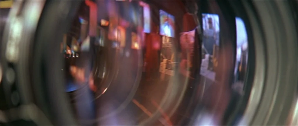 The Moon in the Gutter (1983) movie still: closeup — A macro shot through the circular glass elements of a camera lens. Internal reflections create…