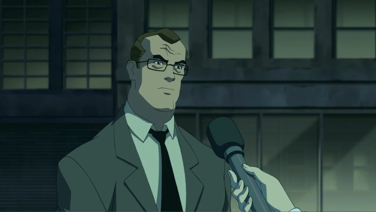 Batman: The Dark Knight Returns, Part 1 (2012) movie still: medium — A man in a suit is interviewed on a city street at night. A microphone is…