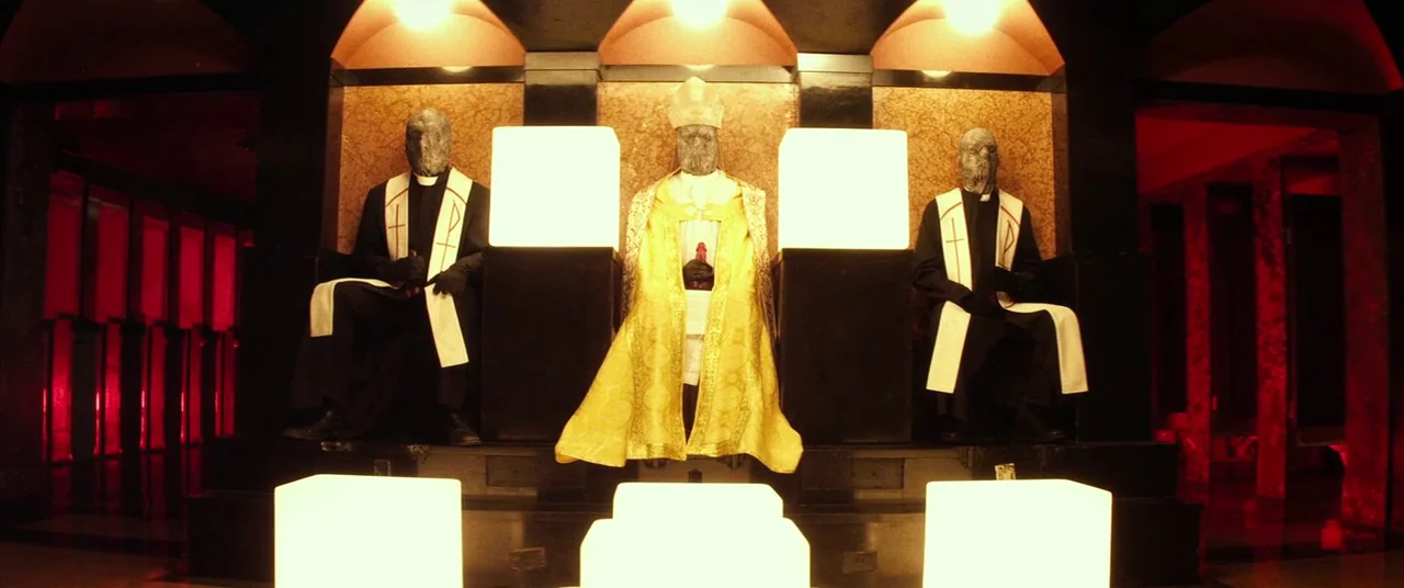 Lords Of Salem (2013) movie still: fullbody — A dark, symmetrical chamber features three throne-like seats highlighted by glowing white cubes. Three…