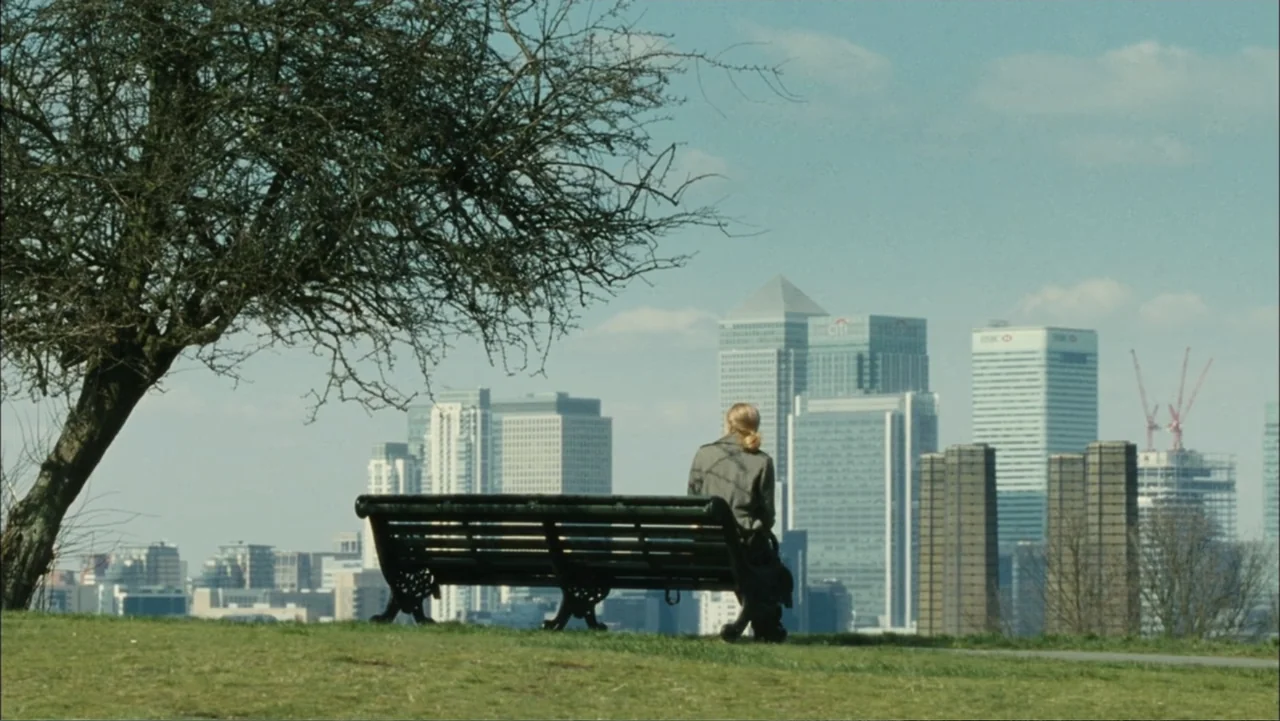 Before I Go to Sleep (2014) movie still: wide — A grassy hill in a public park overlooking a dense modern financial district. A lone person sits on…