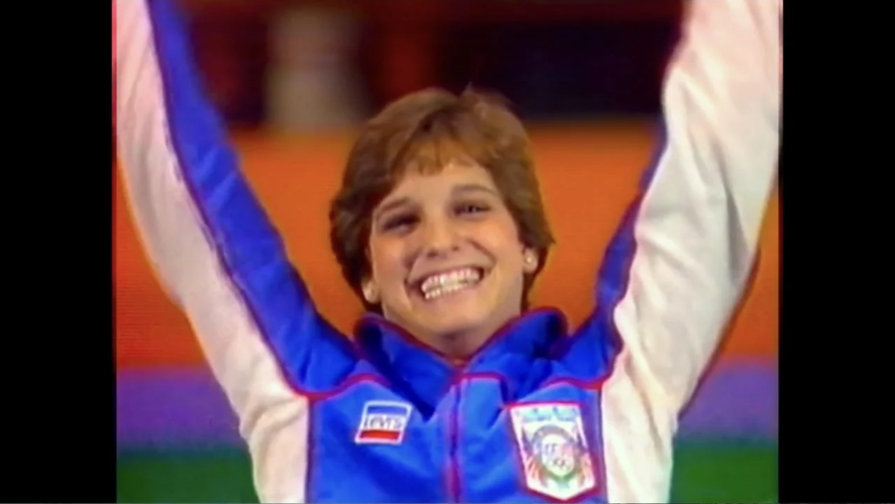 At the Heart of Gold: Inside the USA Gymnastics Scandal (2019) movie still: medium — An indoor venue with bright, saturated color blocks visible in…