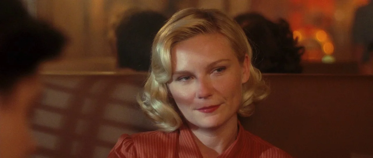 On The Road (2012) movie still: closeup — A dimly lit diner booth at night with a blurred background of other patrons. A woman with blonde wavy hair…