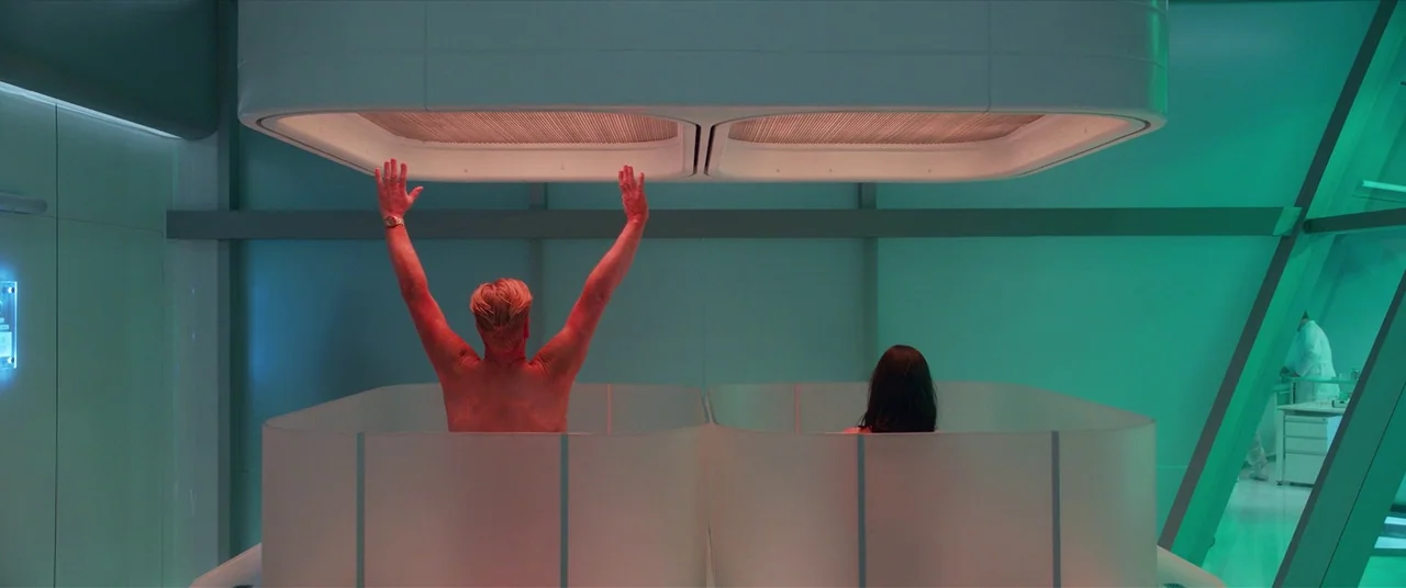 The Predator (2018) movie still: wide — A futuristic clinical room features two people sitting in translucent tubs under light panels. The man…