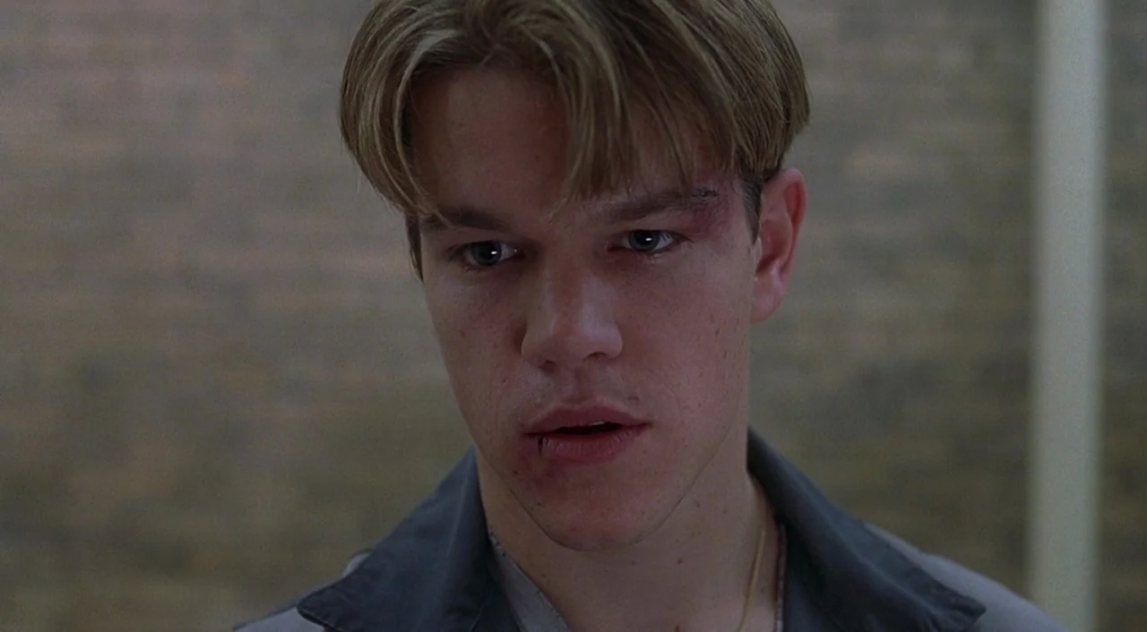 Good Will Hunting (1997) movie still: closeup — A dimly lit indoor hallway with a textured, blurred wall in the background. A young man with facial…