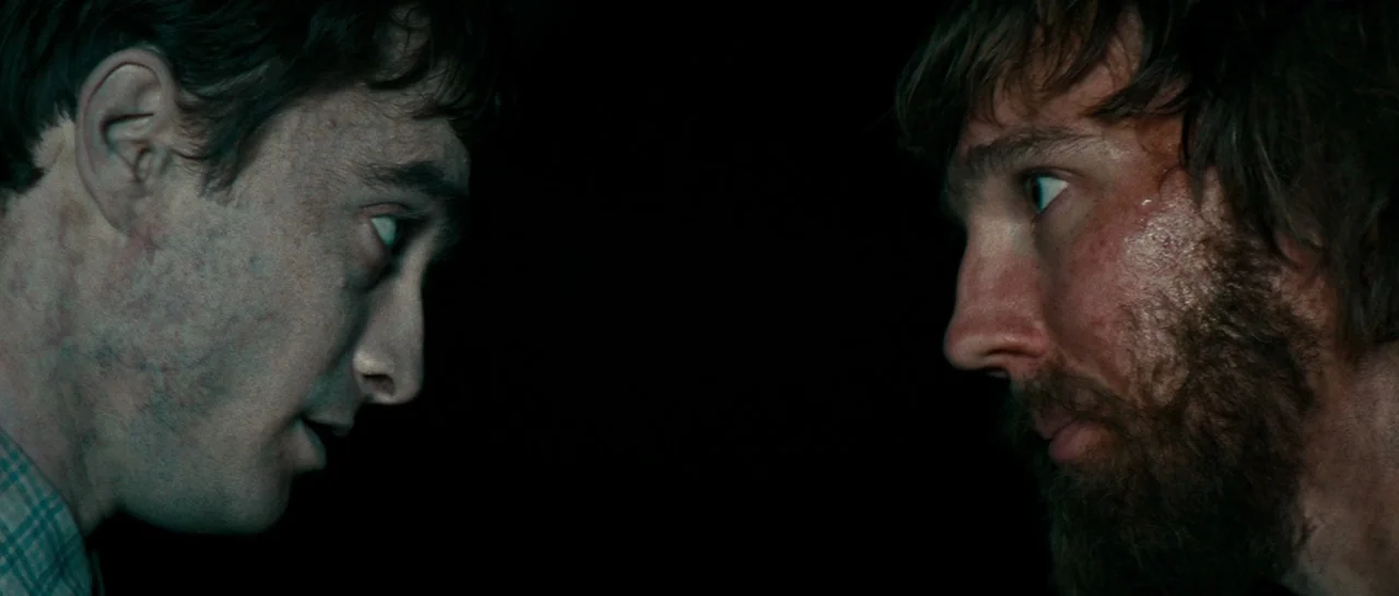 Swiss Army Man (2016) movie still: medium — Two men stand facing each other in a pitch-black setting. They are illuminated from the side in a sharp…