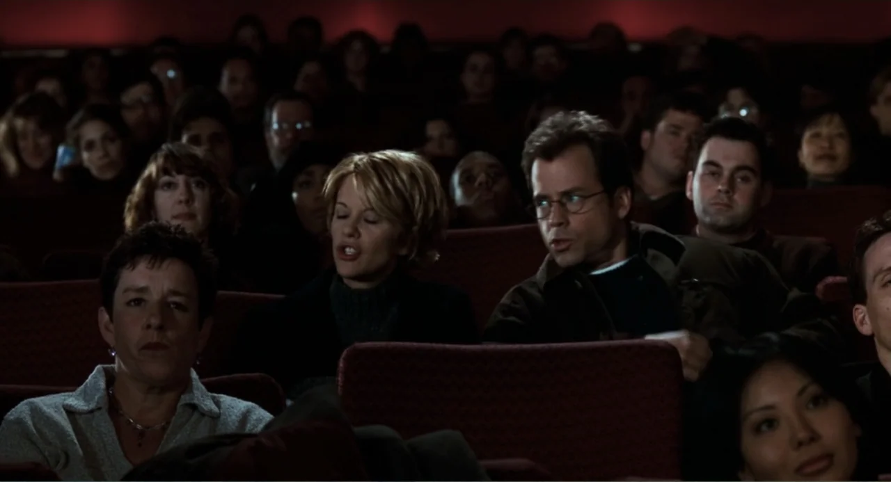 You've Got Mail (1998) movie still: medium — A dark movie theater with rows of occupied red upholstered seats. A man and a woman in the foreground…