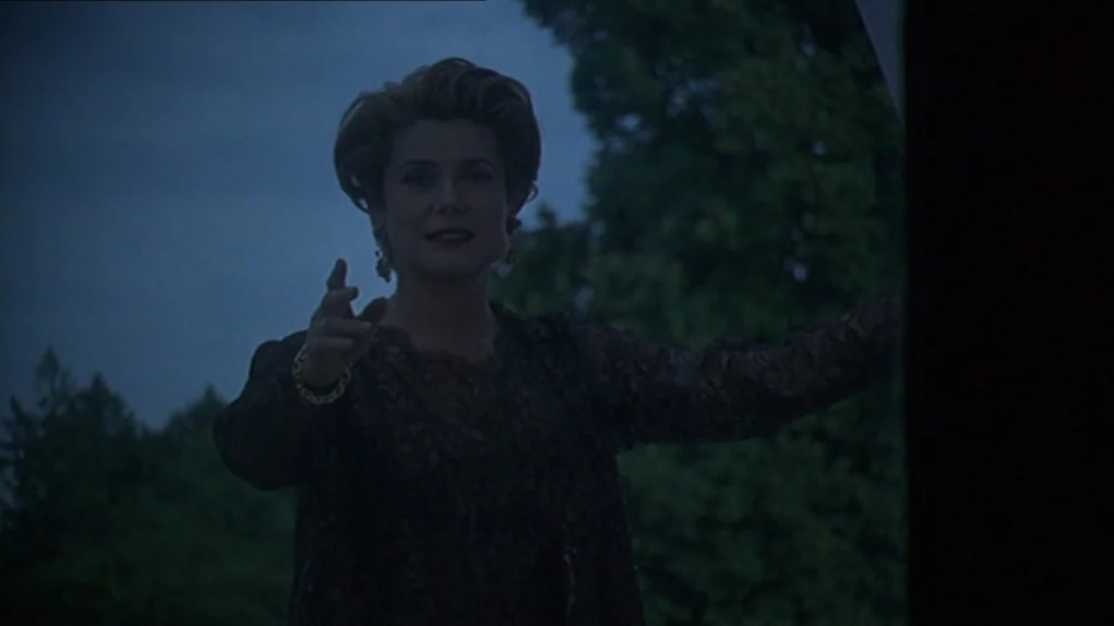 One Hundred and One Nights (1995) movie still: medium — A dark outdoor balcony at night framed against a backdrop of blurry green trees. A woman in…