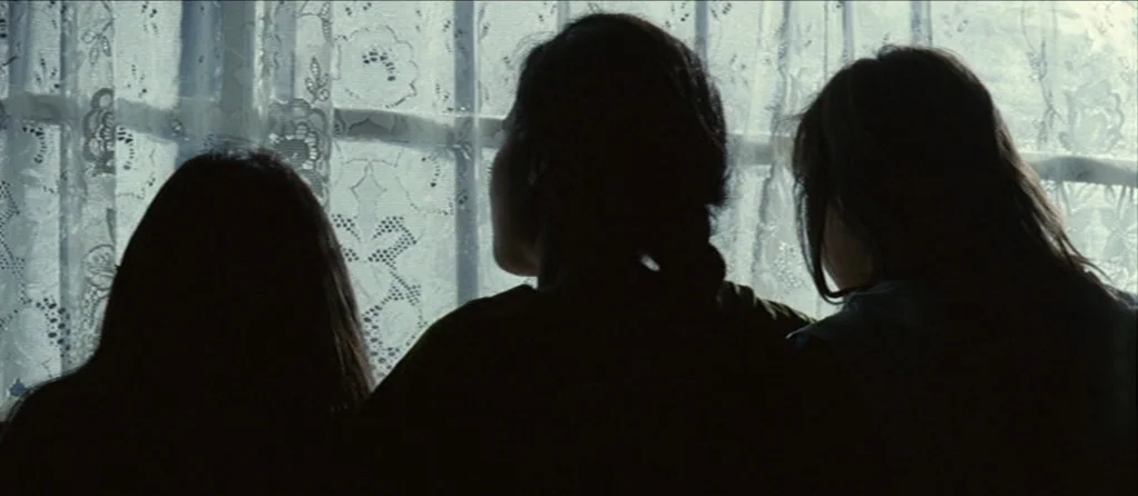 Brick Lane (2007) movie still: medium — Three individuals viewed from behind sit before a window with intricate floral lace curtains. Their…