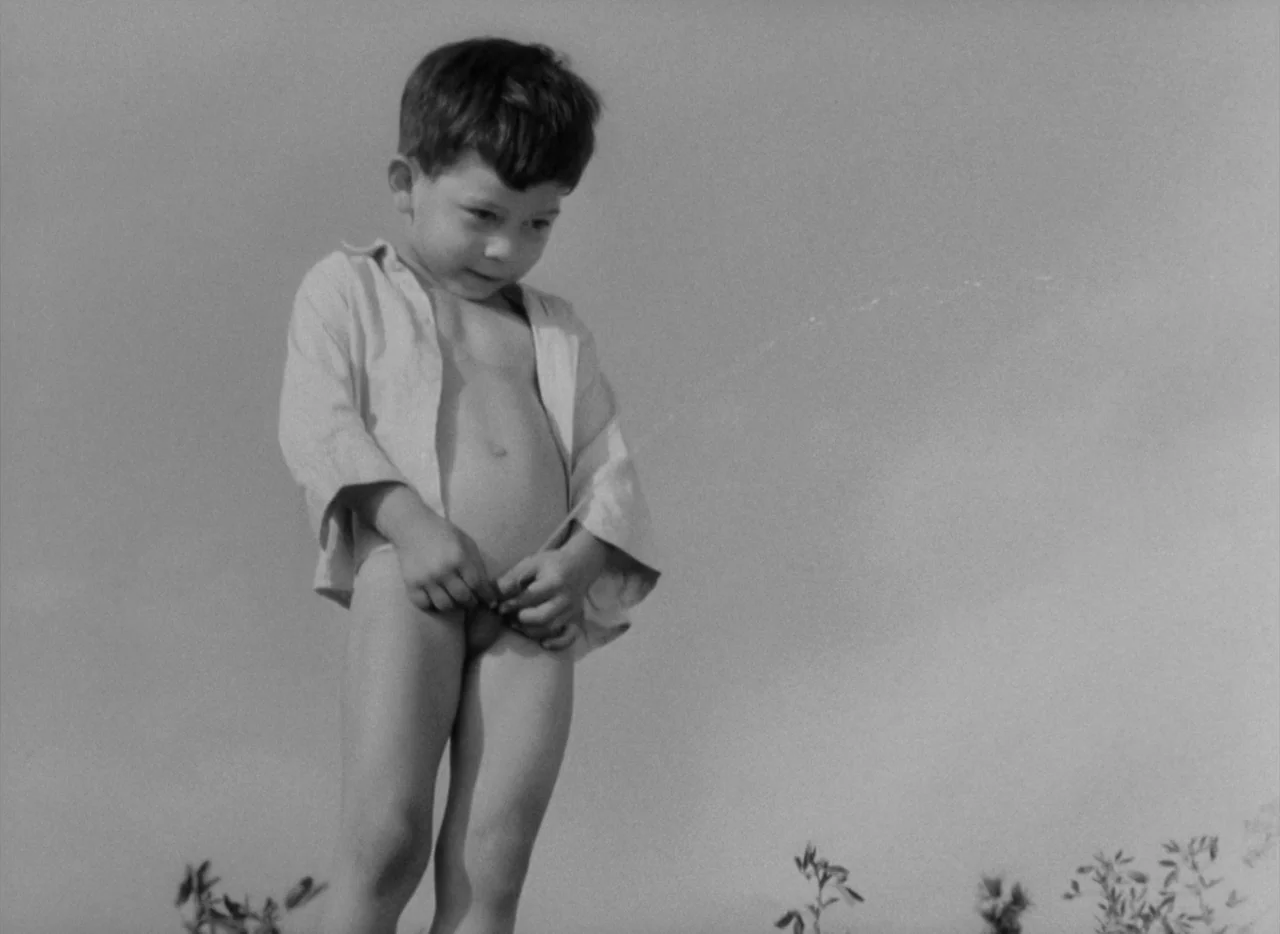 Pearls of the Deep (1965) movie still: fullbody — An open field with sparse vegetation fills the frame under a clear sky. A young boy stands alone…