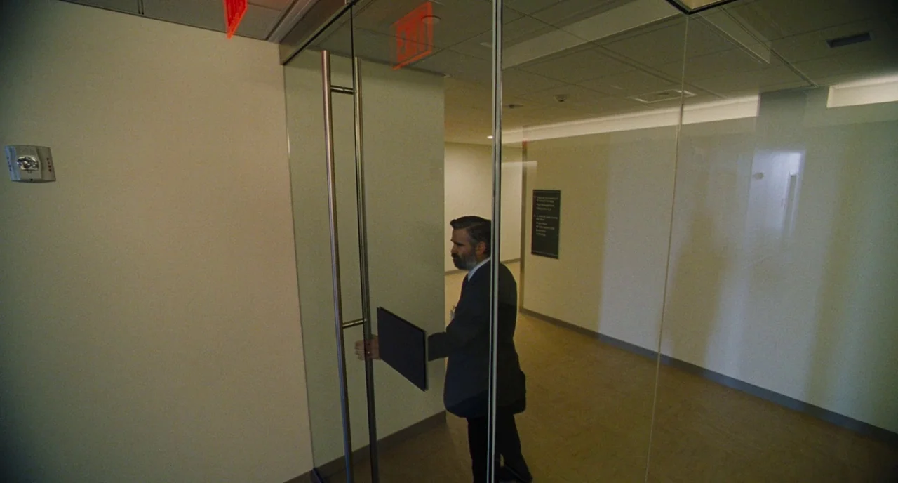 The Killing of a Sacred Deer (2017) movie still: medium — A modern commercial corridor with beige walls and drop ceiling panels. A man in a dark…
