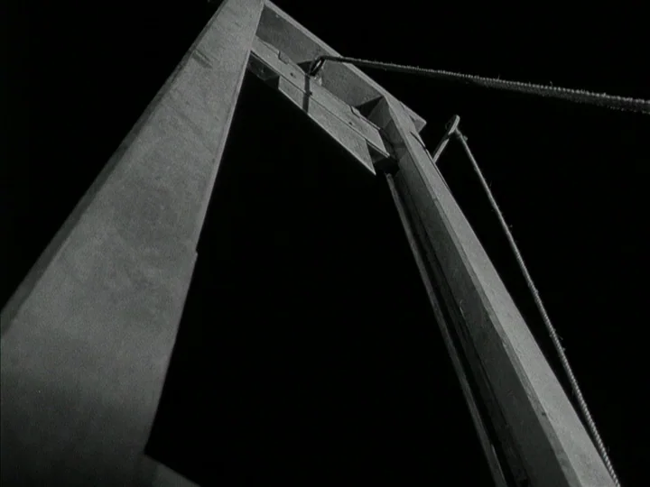 The Black Book (Reign of Terror) (1949) movie still: fullbody — A wooden guillotine frame stands against a dark, featureless night background. The…
