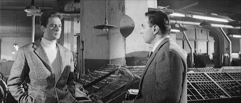 I Vampiri (1957) movie still: medium — A spacious industrial print room contains multiple metal typesetting cases and overhead industrial lamps. Two…