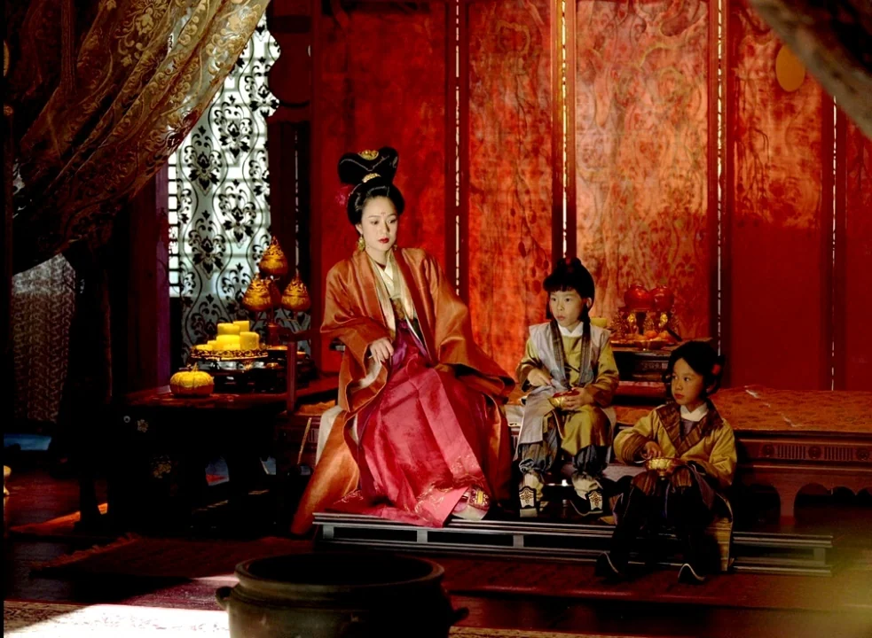 The Assassin (2015) movie still: fullbody — An ornate interior chamber features red wall panels and decorative lattice screens. A woman and two…