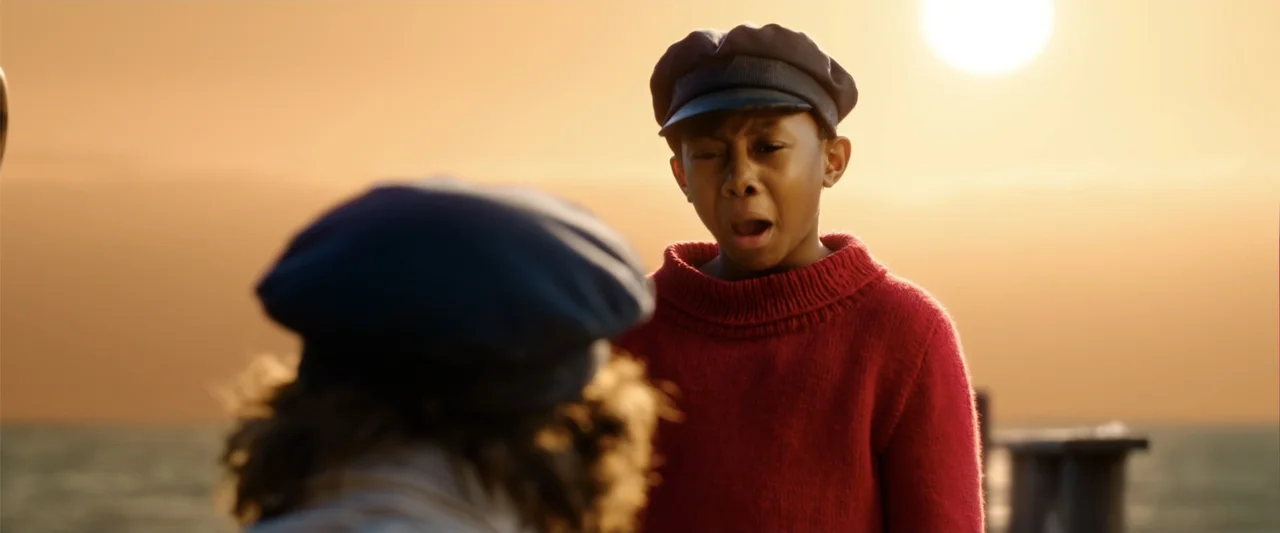 Jim Button and Luke the Engine Driver (2018) movie still: medium — A wooden pier extends into the sea under a bright setting sun. A young boy in a…