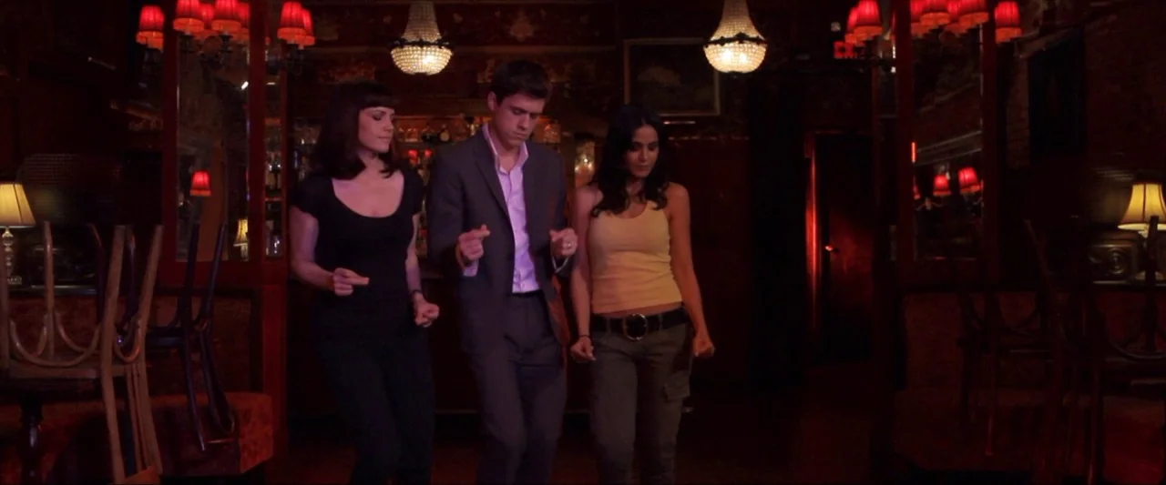 Girl Walks Into a Bar (2011) movie still: fullbody — A dimly lit bar interior features dark wooden walls and multiple red-shaded hanging lamps.…