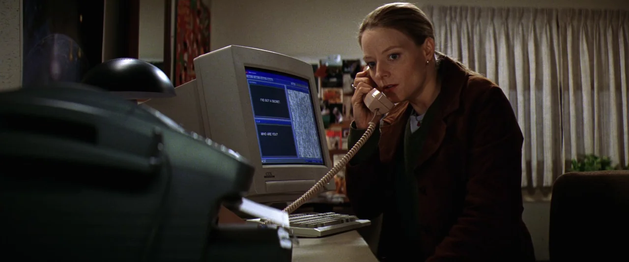 Contact (1997) movie still: medium — A dimly lit room features a 1990s desktop computer setup on a desk. A woman sits in front of the terminal while…
