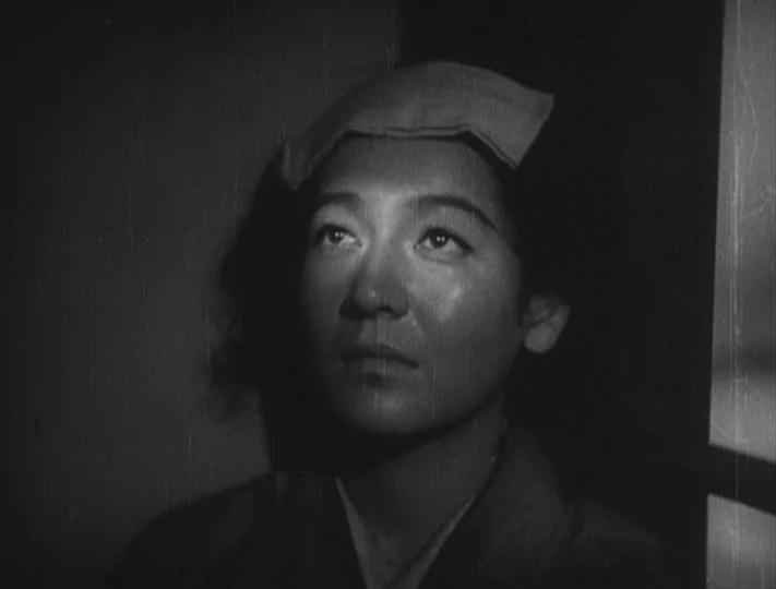 No Regrets for Our Youth (1946) movie still: closeup — A dimly lit room with a vertical wooden screen structure in the background. A woman with a…