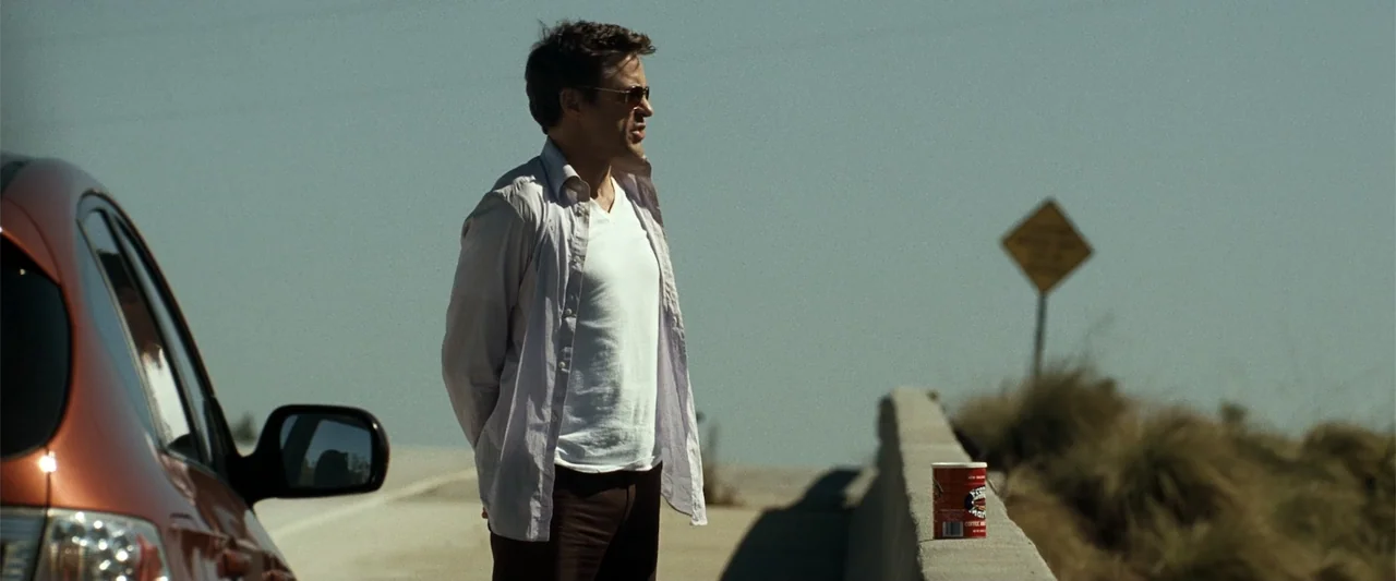 Due Date (2010) movie still: medium — An open highway bridge is visible under clear skies with sparse roadside vegetation. A man in a light shirt…