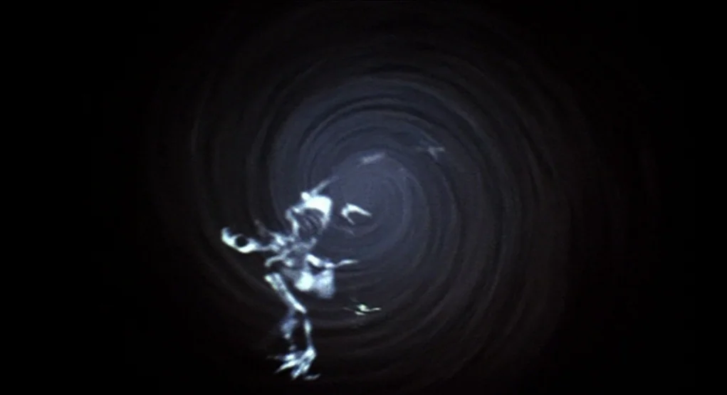 Evil Dead II (1987) movie still: wide — A dark, spiraling tunnel effect creates an impression of movement into an abyss. Light glows faintly from…