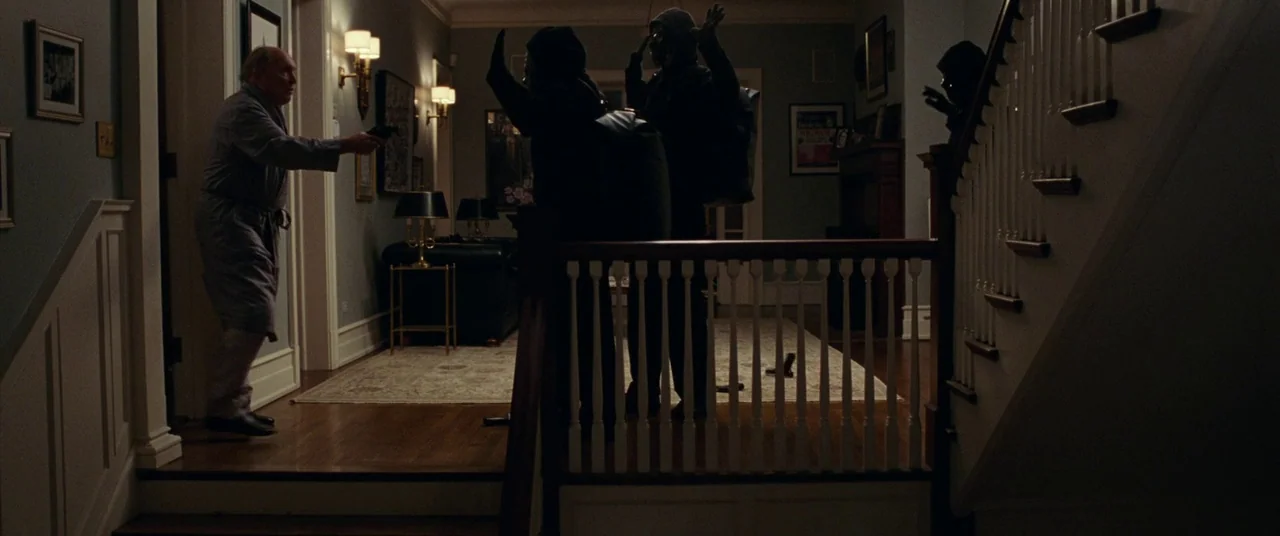 Widows (2018) movie still: wide — A dark, elegant residential entrance hall features pale walls and a polished wood floor. Three masked figures face…