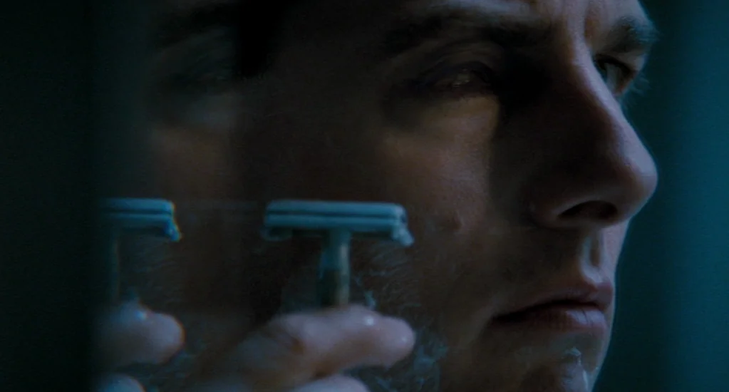 Valkyrie (2008) movie still: closeup — A dimly lit room reflection shows a man's face in a glass surface. He holds a manual razor against his cheek…