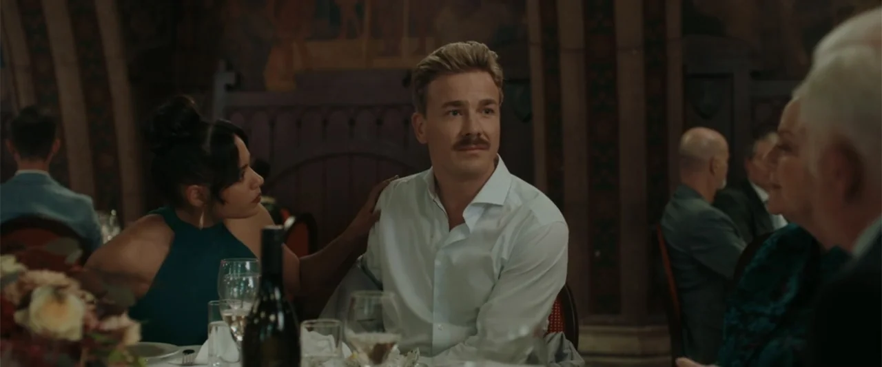 Peacock (2010) movie still: medium — A man and a woman sit at a dining table inside a dimly lit venue. The woman places her hand on the man's…