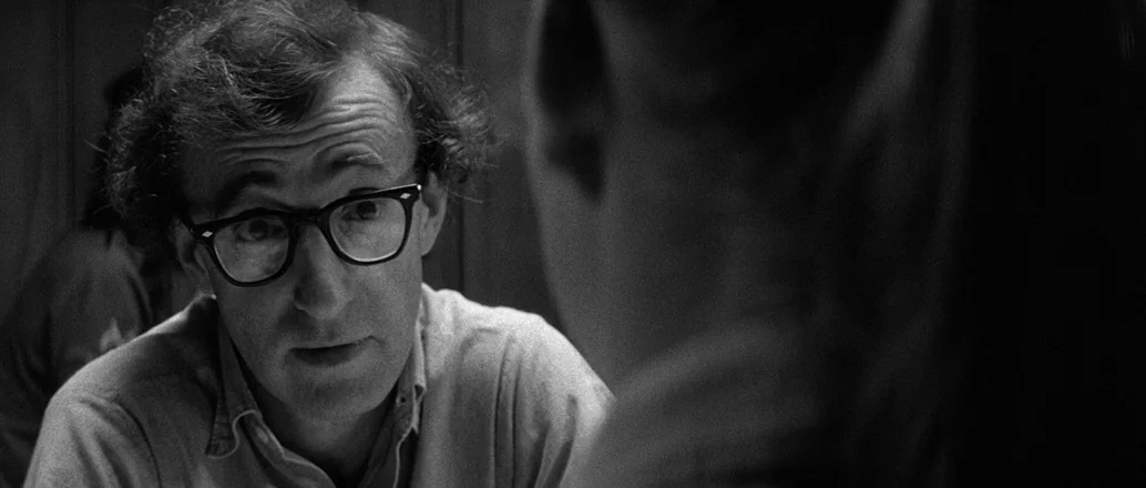 Manhattan (1979) movie still: medium — A man sits at a table in a dimly lit booth. He faces his companion while engaged in a conversation.