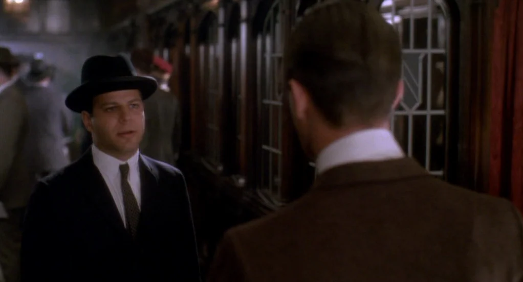 Eight Men Out (1988) movie still: medium — An interior train carriage features dark wood paneling and decorative glass partition windows. A man in a…