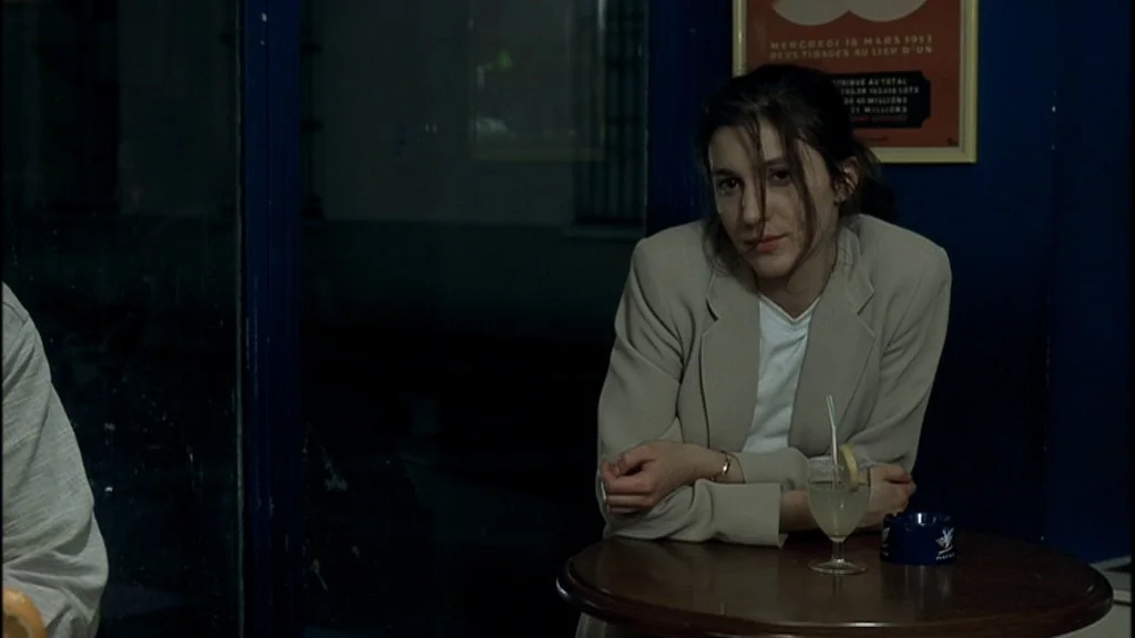 Romance (1999) movie still: medium — A woman sits at a round table inside a dimly lit space at night. She leans forward while a drink and an ashtray…