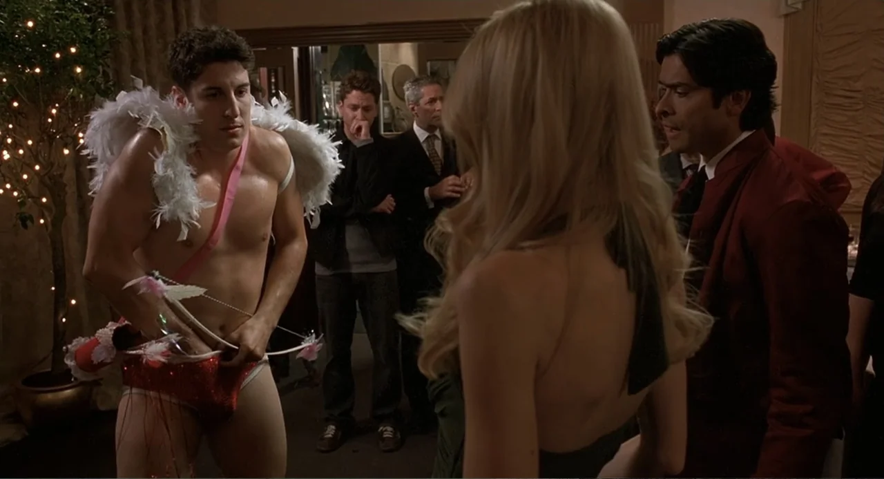 Wedding Daze (2006) movie still: medium — A dimly lit indoor social space featuring guests dressed in formal and costume attire. A man dressed as…