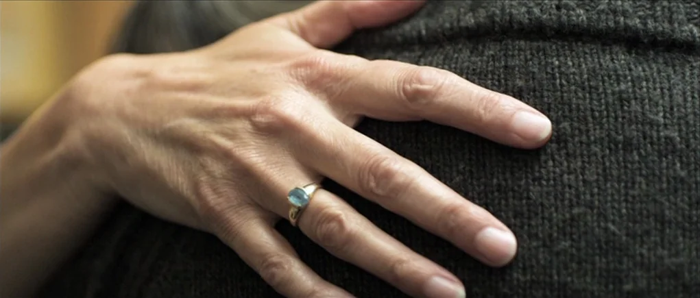 Down Terrace (2009) movie still: closeup — A person's hand rests gently upon the dark textured fabric of a sweater shoulder. A simple gold ring with…