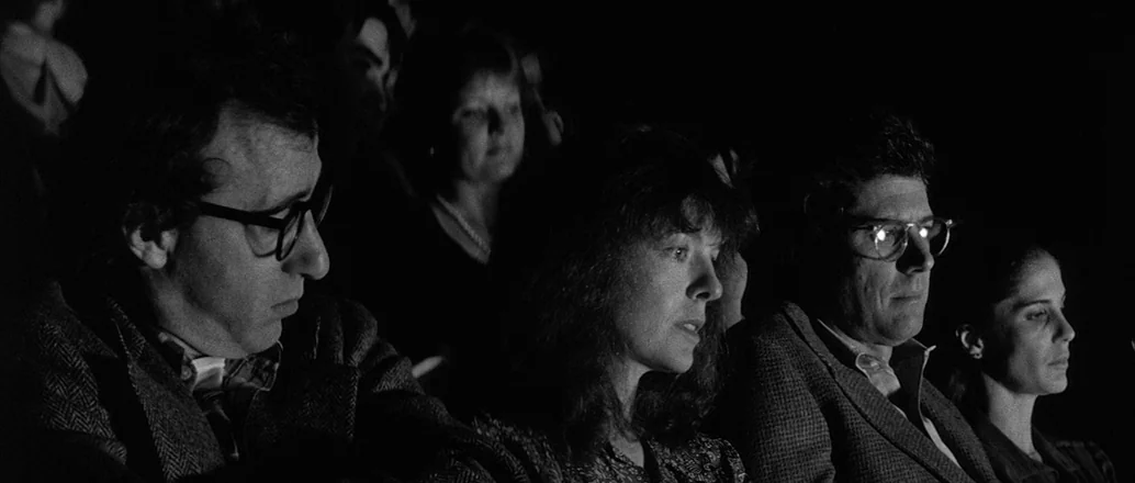 Manhattan (1979) movie still: medium — A group of people sit in a dark room illuminated by reflected screen light. The subjects are arranged…