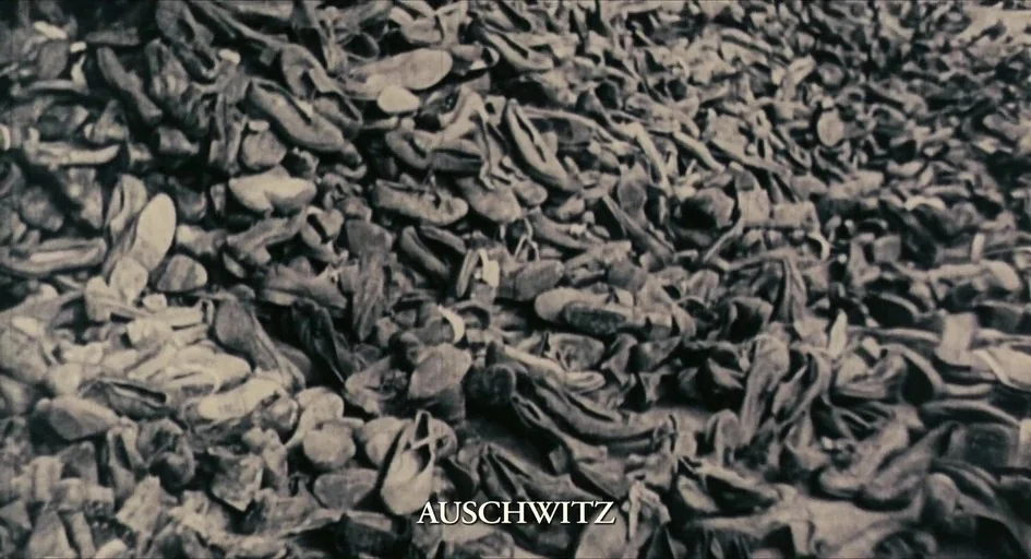 The Last Days (1998) movie still: establishing — A dense, chaotic pile of thousands of worn leather shoes fills the frame. The word Auschwitz is…