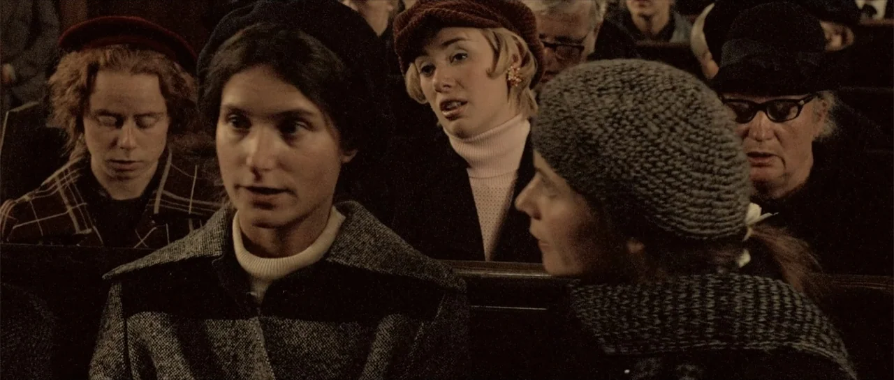 Breaking the Waves (1996) movie still: medium — A group of people sit together on wooden benches inside a dimly lit room. The primary subject…