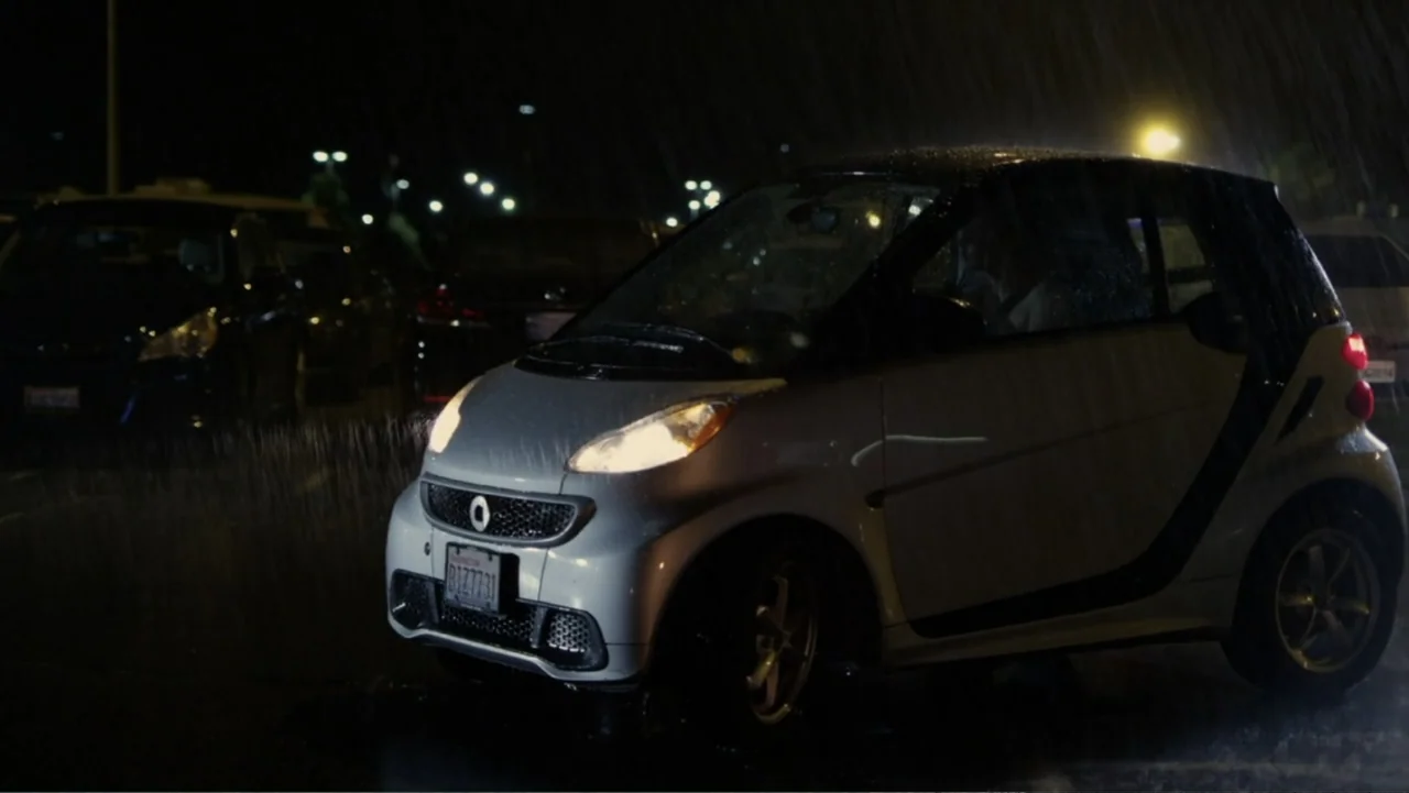 Hogar, dulce hogar (1941) movie still: medium — A silver compact car sits in a dark parking lot during a rainstorm. An individual sits in the driver…