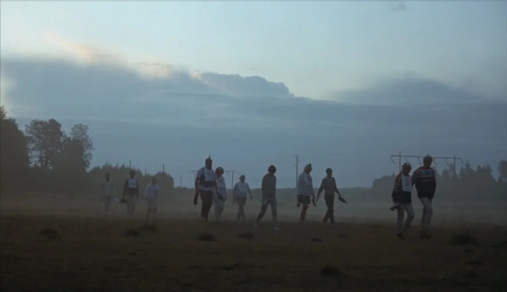 A Swedish Love Story (1970) movie still: wide — A group of people walks across a flat, fog-covered field during early morning. Power lines and dark…