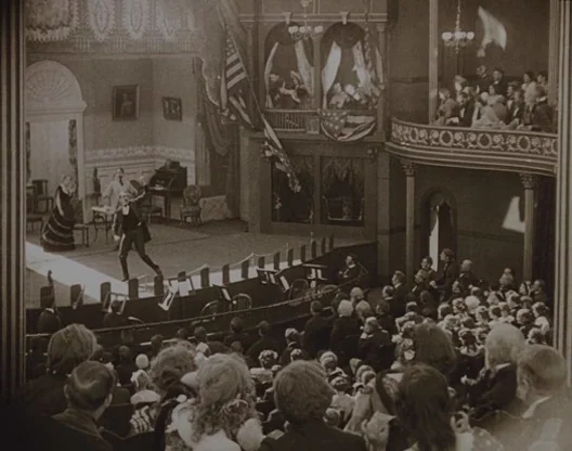 Birth of a Nation (1915) movie still: wide — An ornate 19th-century theater features tiered seating, private boxes, and a large central stage. A…
