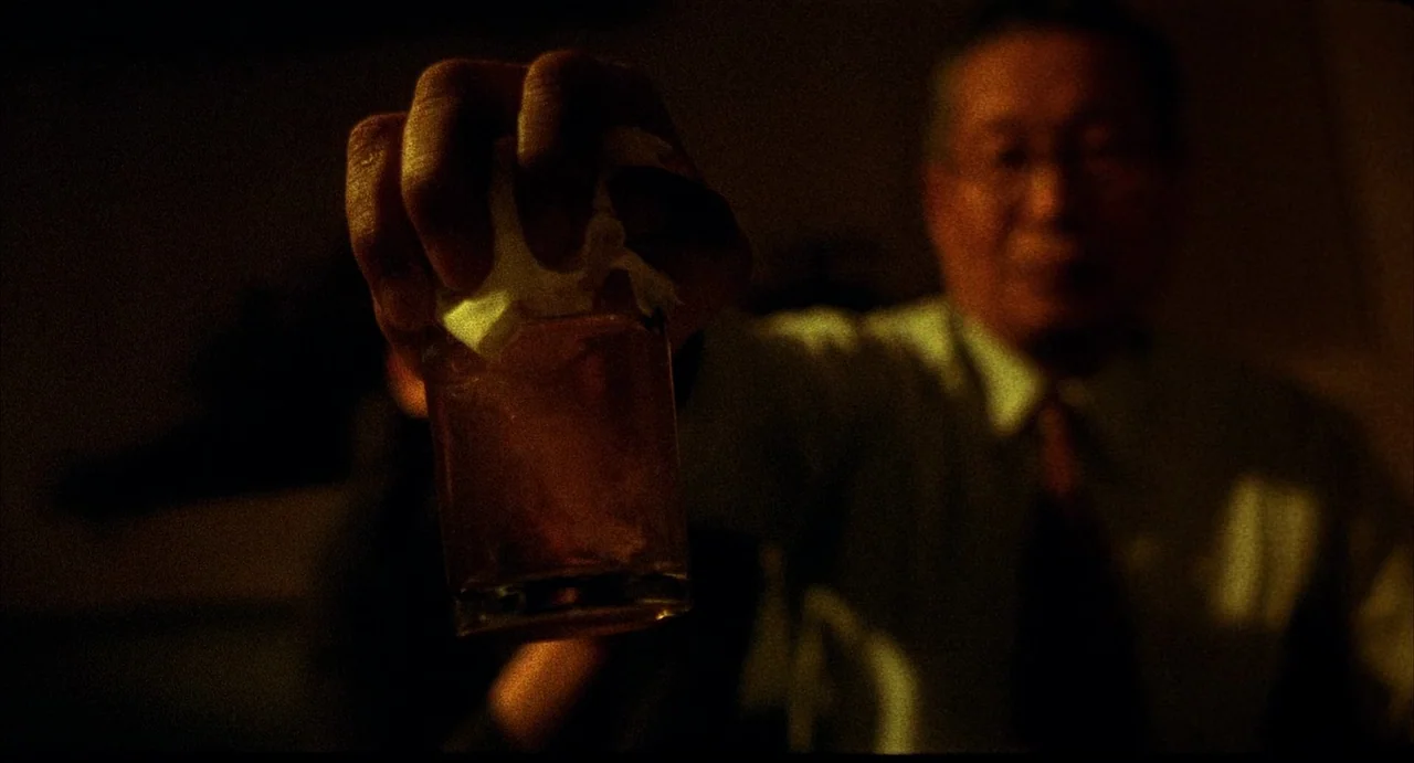 Barking Dogs Never Bite (2000) movie still: closeup — A dark dimly lit bar interior creates a low-key atmosphere with heavy shadows. An elderly man…
