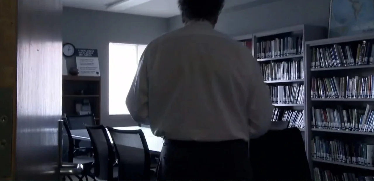 Doctors of the Dark Side (2011) movie still: medium — A quiet library room with tall bookshelves and a table with chairs near a window. A man in a…