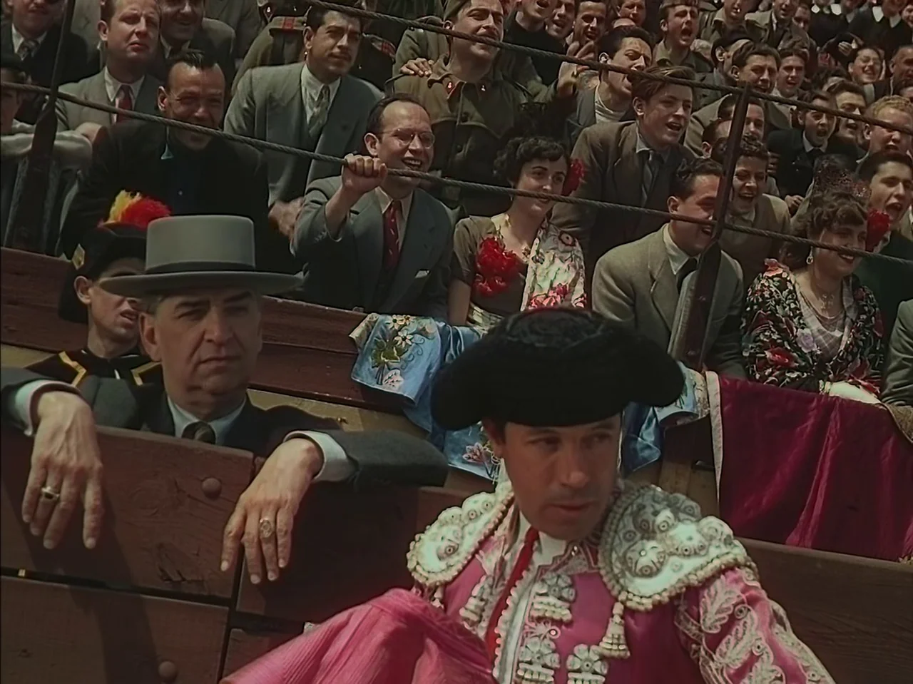 Pandora and the Flying Dutchman (1951) movie still: medium — A tiered outdoor arena with wooden benches filled with a large crowd of spectators. In…