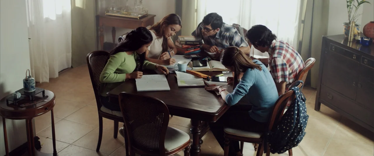 La Musiquita por Dentro (2019) movie still: medium — A group of five students studies at a large dark wood dining table. They are writing in…