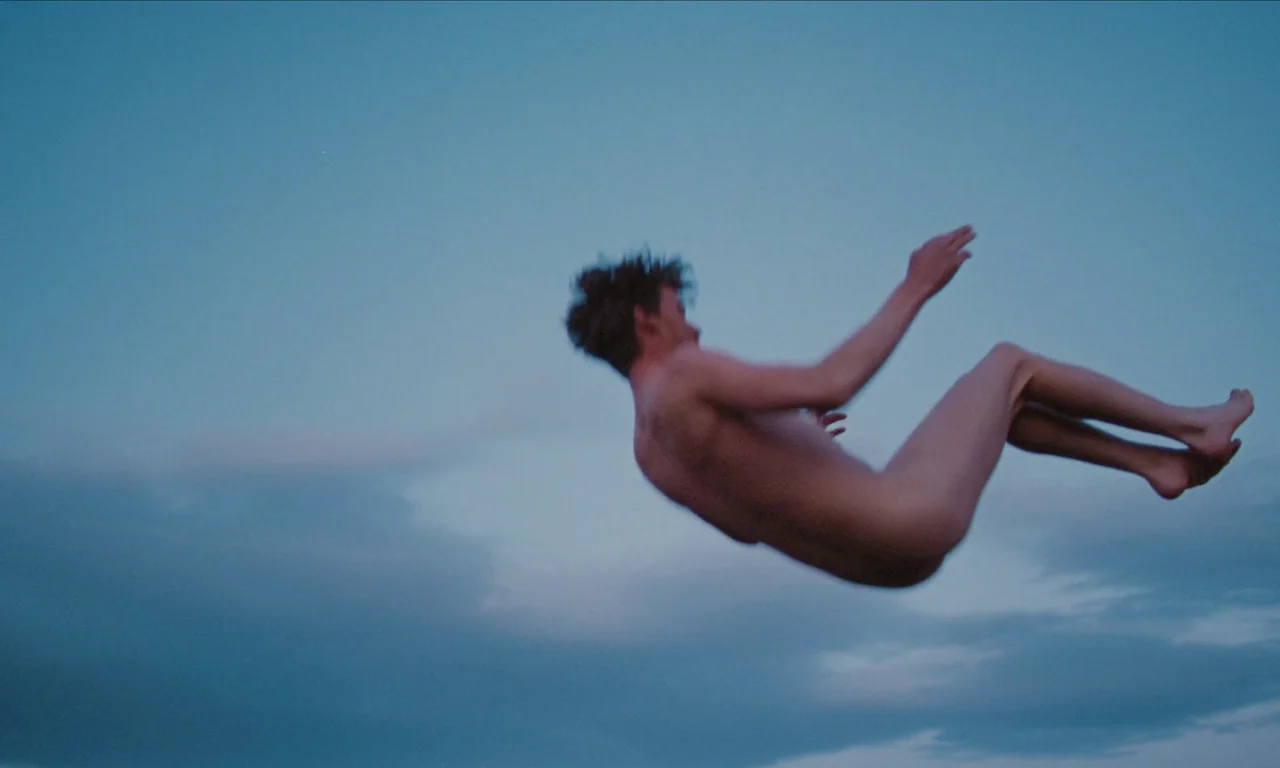 National Anthem (2023) movie still: fullbody — A man moves through the air against a twilight blue sky with faint clouds. He is suspended in mid-air…