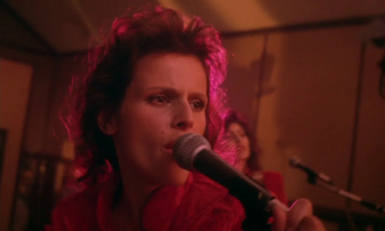 Paganini Horror (1989) movie still: closeup — An interior recording studio features acoustic foam walls bathed in deep red light. A woman with…