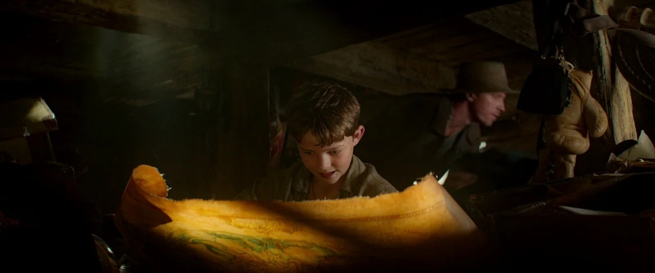 Pan (2015) movie still: medium — An attic space filled with wooden beams and clutter illuminated by dusty window light. A young boy holds an open…