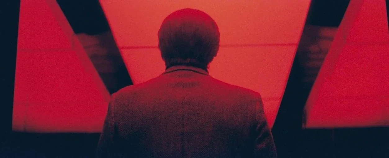 Beyond The Black Rainbow (2010) movie still: medium — A man stands before a bright, intensely red illuminated surface in a dim space. He is centered…