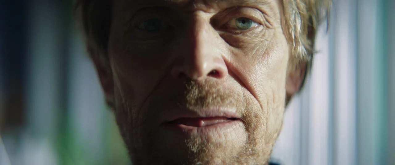 Inside (2023) (2023) movie still: closeup — A man's face occupies the frame against a blurred background of vertical blinds. The subject stares…