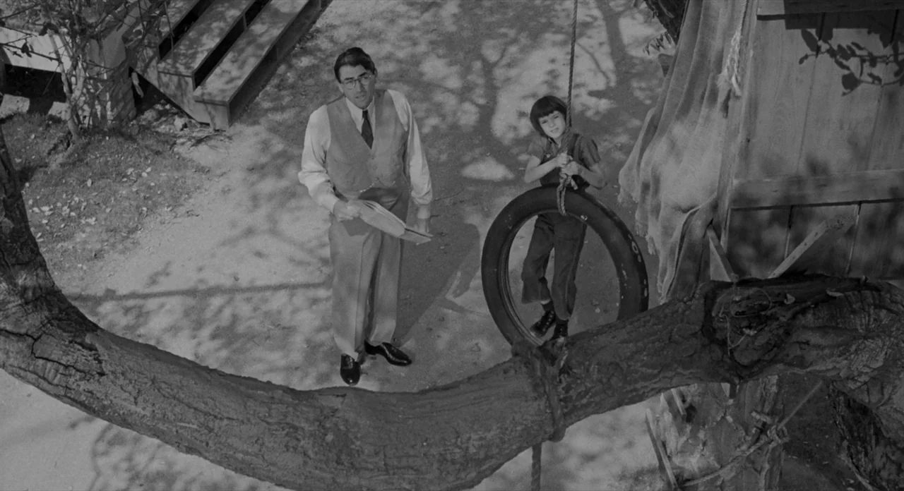 To Kill A Mockingbird (1962) movie still: fullbody — A backyard setting featuring a dirt ground and a large tree limb overhead. An adult man and a…