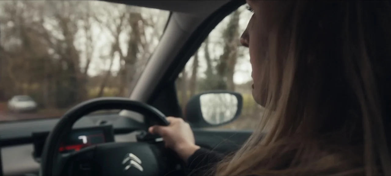 No Woman No Try (2022) movie still: medium — The interior of a modern car shows a driver's perspective of the road ahead. A woman with long hair…