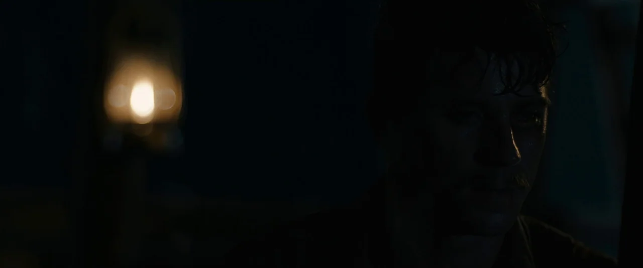 Mudbound (2017) movie still: closeup — A man sits in a dark, poorly lit room with very little visible environmental detail. He looks downward while…